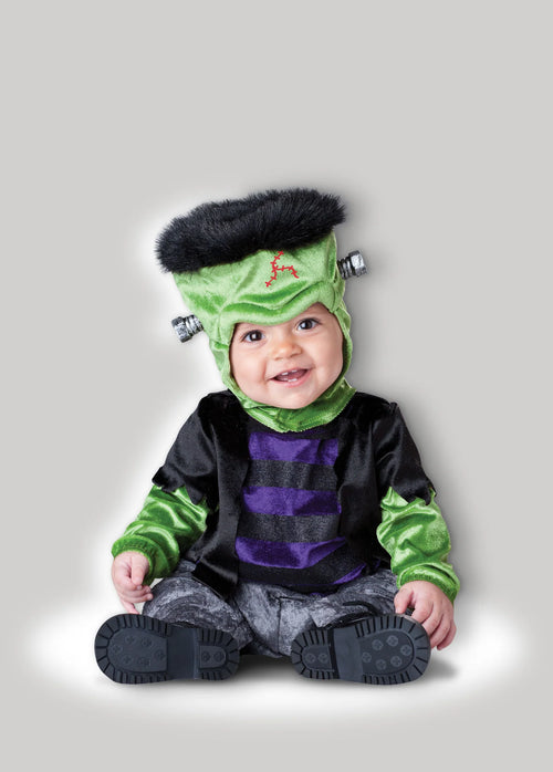 A baby wearing a Frankenstein costume, sitting against a solid gray background. The costume includes a green headpiece with black hair and silver bolts, a black and purple striped shirt, and green striped sleeves, with gray pants and black booties.