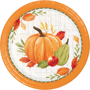A round paper plate with a fall harvest design, featuring an orange pumpkin, green pear, red apple, and autumn leaves on a white patterned background with a bright orange rim.