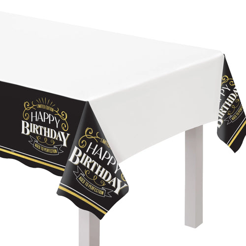 Black 'Happy Birthday' tablecloth with gold text on a white table.