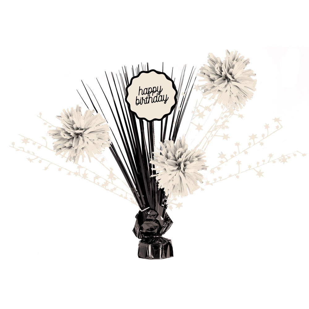 Decorative birthday centerpiece with black sticks, white flowers, and 'happy birthday' sign on a white background