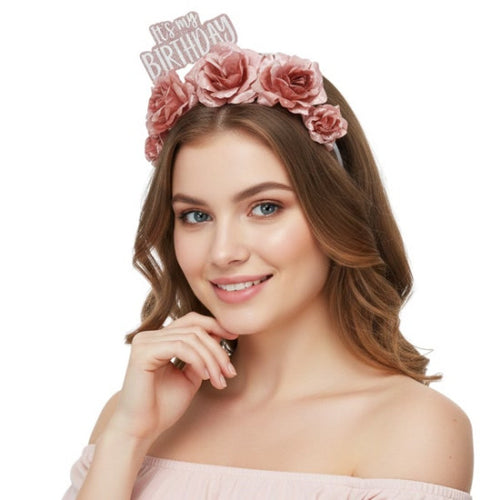 A woman wearing a dusty pink floral crown headband with a silver glitter 'It's my BIRTHDAY' banner, posing against a solid white background.