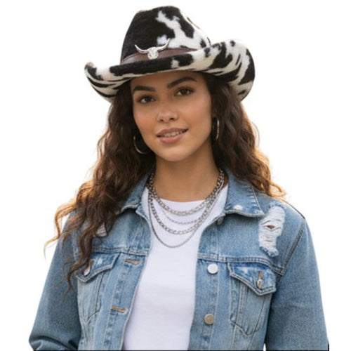 A woman wearing a black and white faux fur cowboy hat with a silver horn emblem, a light blue distressed denim jacket, and a white t-shirt, set against a plain white background.