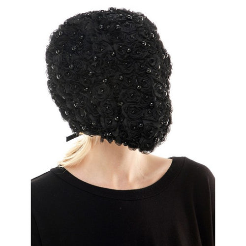 A black textured bonnet or headband with layered rosette flower details and small shiny embellishments, shown on a model from the back against a plain white background.
