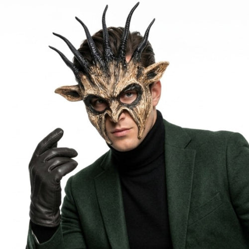 A man wearing a detailed fantasy horned mask with textured brown and black coloring, a black glove, and a dark green blazer over a black turtleneck, set against a plain white background.