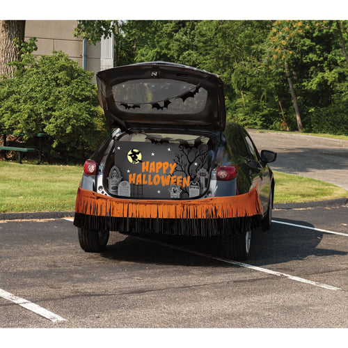 A black car parked in a lot with its trunk open, decorated for Halloween. The back of the car features a black Halloween-themed fabric cover with a fringe bottom, and the words 'HAPPY HALLOWEEN' in orange and white.