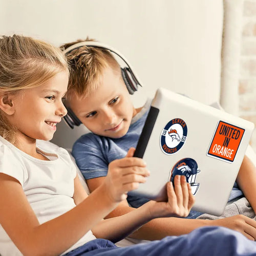 Two children sitting together, one wearing headphones, looking at a tablet with stickers on it.