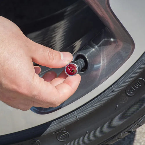 Hand inserting a red valve cap with a logo into a car tire valve.