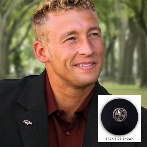 Man wearing a black blazer with a logo, standing outdoors with trees in the background.