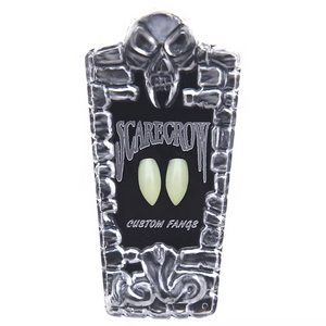 A coffin-shaped display card for 'Scarecrow' custom vampire fangs, featuring a skull and stone border design with two glowing pale green fangs in the center, on a white background.