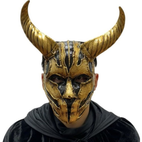 A person wearing a gold and black horned mask with a dark hooded garment, shown against a plain white background.