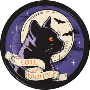 A circular vintage-style illustration featuring a black cat in profile with one orange eye, set against a purple night sky with bats, stars, and a cream moon. A cream banner across the bottom reads 'TOIL and TROUBLE'.