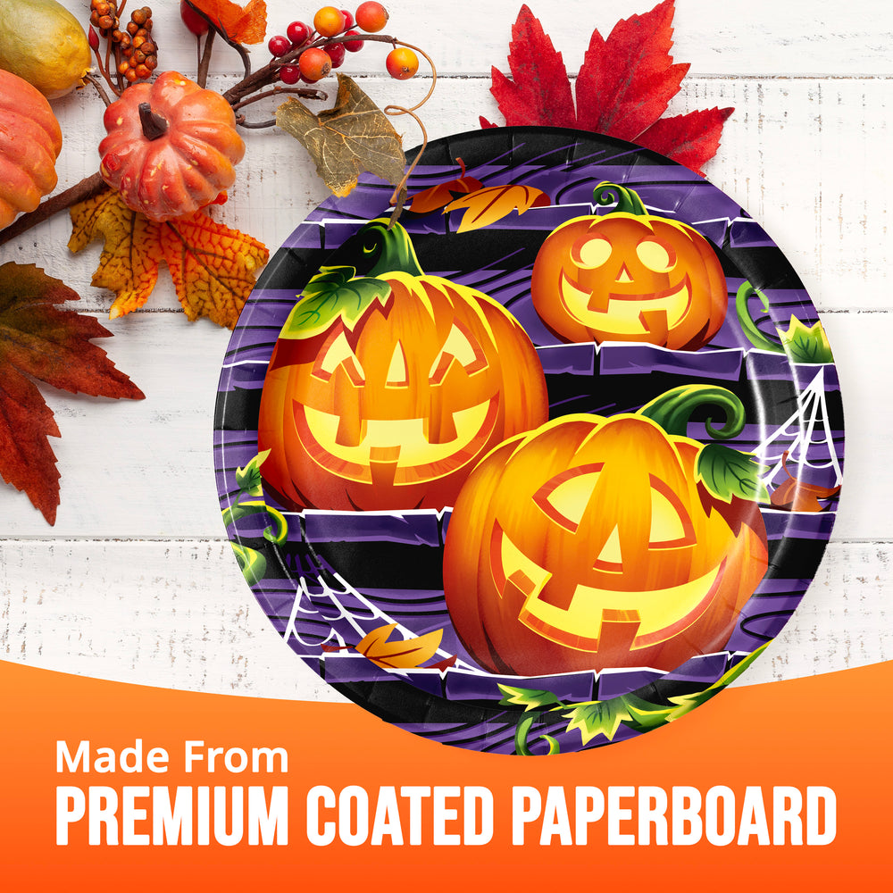 Halloween-themed paper plates with carved jack-o'-lantern illustrations on a purple background, styled with autumn leaves and pumpkins on a white wood surface, with an orange banner reading 'Made From PREMIUM COATED PAPERBOARD'.
