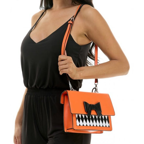 An orange shoulder bag with a black and white harlequin patterned front panel and a black bow accent, shown being worn by a model in a black jumpsuit against a white background.