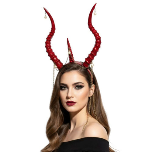 A woman wearing a red devil horn headband with long curved horns, gold chain details, and small pearl-like drops against a plain white background.