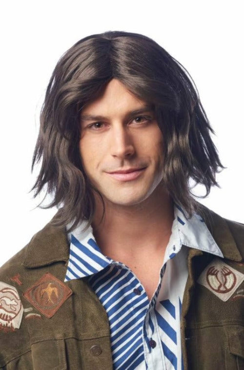 A man wearing a medium-length, shaggy dark brown wig with side-swept bangs, styled with a brown jacket and a blue-and-white striped shirt against a plain white background.