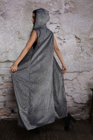 Person wearing a long, dark gray hooded garment against a textured stone wall.