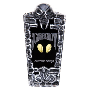 A tombstone-shaped custom fan sign featuring a black center with the words 'SCARECROW' and 'CUSTOM FANGS' in stylized white lettering, flanked by two gold oval eyes, and framed by a silver skull and stone border at the top and bottom.