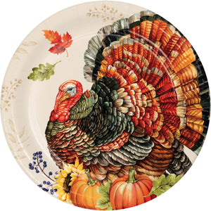 A round paper plate featuring a detailed illustration of a Thanksgiving turkey with orange, red, brown, and black feathers, surrounded by autumn leaves, pumpkins, and sunflowers on a cream background.