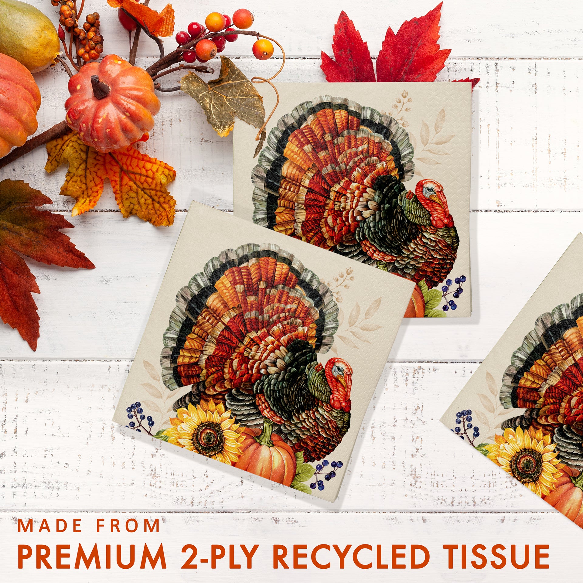 Three square decorative tissue paper napkins featuring a colorful autumn turkey design, arranged on a white wood background with fall leaves, pumpkins, and berries. Text at the bottom reads 'MADE FROM PREMIUM 2-PLY RECYCLED TISSUE'.