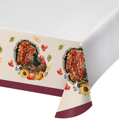 A white tablecloth with a printed autumn turkey and fall leaves pattern along the border, shown draped over a table corner against a white background.