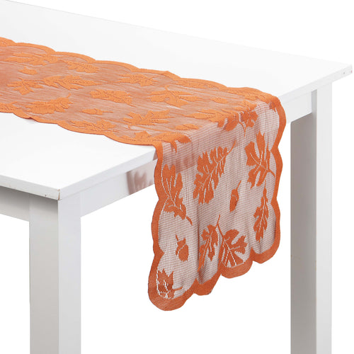 An orange lace table runner with a scalloped edge and leaf pattern draped over a white table against a white background.