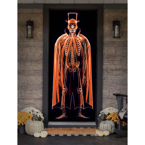 A Halloween-themed door decoration featuring a glowing orange skeleton figure wearing a top hat and cape on a black background, displayed on a front door with stone walls, lanterns, pumpkins, and fall flowers.