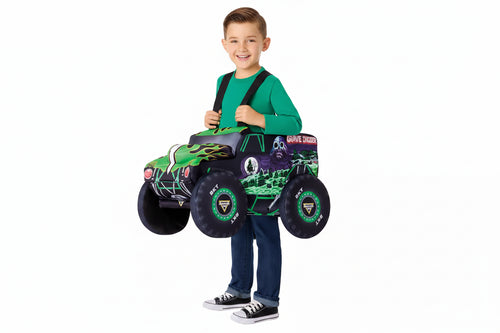 A young boy wearing a Monster Trucks 'Grave Digger' costume stands behind a toy ride-on truck, holding the handle. The costume includes a black cap with a 'Monster Trucks' logo, a green long-sleeve shirt, and blue jeans.