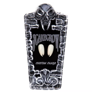 A pair of custom vampire fangs displayed on a black tombstone-shaped stand with a skull and the words 'SCARECROW' and 'CUSTOM FANGS' on a white background.