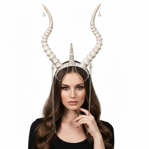 A woman wearing a horned headpiece with tall curved ivory horns, a central horn, dangling chains, and small teardrop charms against a plain white background.